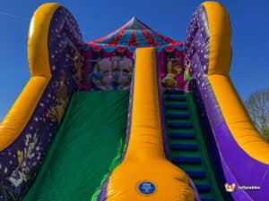 A colorful inflatable slide with vibrant purple and yellow accents, featuring cartoon characters, under a blue sky.