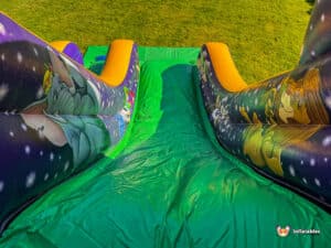 A vibrant inflatable slide with colorful character designs, set on green grass and featuring a smooth, shiny sliding surface.