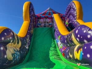 A colorful inflatable slide with yellow edges and cartoon characters, set against a clear blue sky.