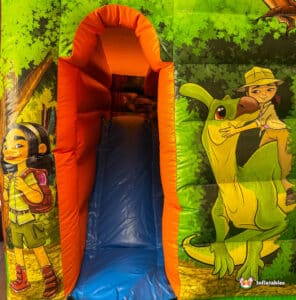 A colorful inflatable slide featuring jungle-themed artwork, including a girl with a backpack and a playful green dinosaur.