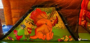 A colorful inflatable tent featuring a cartoon boy with a camera and a friendly triceratops in a vibrant, nature-themed design.