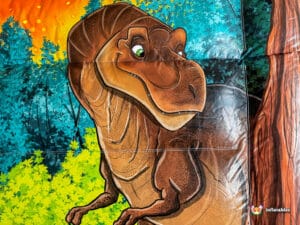 A cartoon-style T-Rex smiles amid vibrant forest scenery, featuring bright green foliage and a fiery orange backdrop.