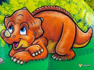 A cheerful cartoon triceratops with large blue eyes and a big smile, set against a vibrant green background with yellow foliage.