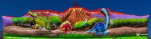 Colorful inflatable dinosaur scene featuring a volcano, lush greenery, and three distinct dinosaur figures against a clear blue sky.