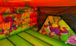 Inside a colorful dinosaur-themed bounce house, featuring playful cartoon characters engaging with various dinosaurs on bright walls.