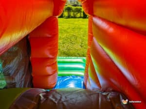 View from inside a colorful bounce house, showing vibrant orange walls and a bright green exterior lawn in sunlight.