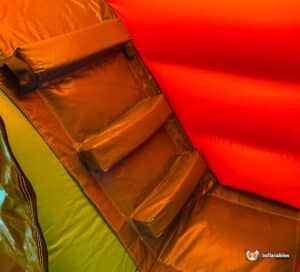 Interior close-up of a colorful inflatable structure, featuring padded seating and vibrant orange and green walls.