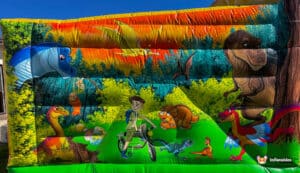 A colorful inflatable backdrop depicts a scene with dinosaurs, a boy on a bicycle, and lush greenery against a bright sky.