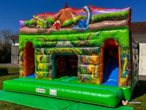 A vibrant inflatable dinosaur double slide cabin with a dinosaur theme, featuring colorful illustrations and a slide, set on a sunny lawn.