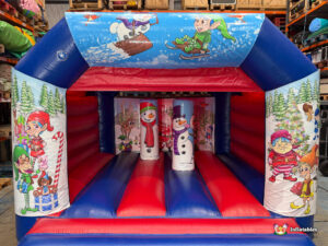 Full frontal view of a red and blue inflatable bouncy castle featuring a Christmas theme with illustrations of Santa's elves, snowmen, and winter scenes