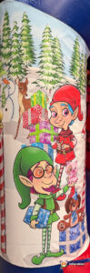 Close-up side art of the bouncy castle featuring two different elves—one in red and one in green—standing next to stacks of gifts, a deer, and snowy trees.
