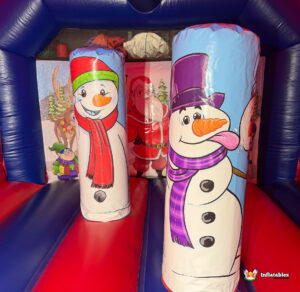 Interior shot of the bouncy castle showing the two snowman-themed inflatable pillars standing on the bouncing floor, with a large Santa illustration visible on the back wall.