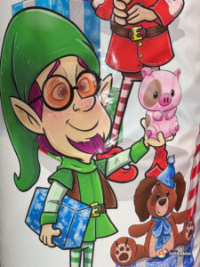 Extreme close-up of the side art showing a green-hatted elf with glasses holding a blue gift and a small pink toy pig.