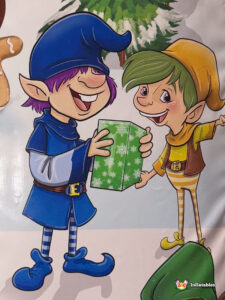 Close-up artwork featuring two cartoon elves—one in blue and one in yellow—happily exchanging a green gift box with white snowflakes.