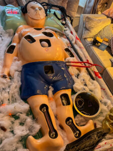 Close-up overhead shot of the Halloween operation game board, clearly showing the game holes, the Jason-style hockey mask, the red operating wire/tool, and the fake spiderwebs covering the setup.