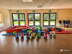 Close-up of children's soft play equipment set up in the main hall, featuring a large ball pit, colorful foam blocks, and a row of small ride-on cars.