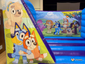 Angled close-up of the left side of the inflatable, showing Bluey, Bingo, and Mackenzie on the front panel and a larger group of Bluey characters on the back wall.