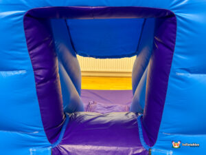 Interior close-up looking through the purple-lined pop-up exit hole of the blue inflatable, showing the purple safety mat on the ground below.