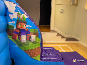 Close-up of the entrance to the slide ramp, featuring a blocky character sitting down with a small frog/lizard mob on their head, ready to slide down the purple ramp.