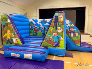 Angled view of the Minecraft Bounce and Slide inflatable, showing the entrance pad and the entire structure with blocky character art, including a Zombie, Enderman, and Steve.
