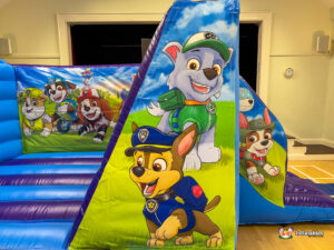 Angled view of the right side of the inflatable, showing artwork of Rocky and Chase on the side barrier, and the group image of the pups on the back wall.