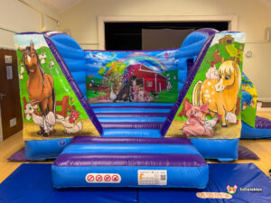 Direct frontal shot of the inflatable, emphasizing the wide entrance step and the central mural of a red barn, rainbow, and various farm animals on the back wall.