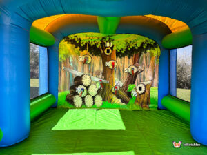 An interior shot of the inflatable axe throwing arena looking toward the back wall mural which features circular wood-cut targets with point values like 50, 75, and 100.