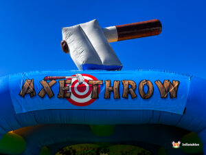 A close-up of the top banner of the arena, featuring the words "AXE THROW" in wooden-style letters over a target graphic, with a large 3D inflatable axe resting above it.