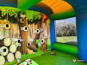Interior shot of a red and yellow foam axe in mid-air, flying toward a forest-themed inflatable target wall with point values like 50, 75, and 100.