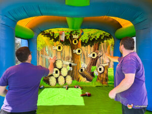 Action shot of two people successfully throwing foam axes at the same time, with the axes shown mid-flight inside the blue inflatable arena.