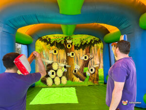 A view from behind two participants as they aim their foam axes at the woodland target wall inside the large blue inflatable structure.