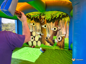 Close-up over the shoulder of a participant as they hold a blue foam axe, focusing on the various circular targets and squirrel illustrations on the arena's back wall.