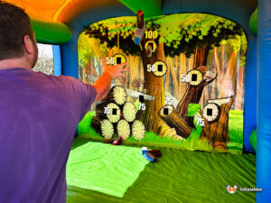A participant throwing a foam axe, which is shown spinning in the air toward the 100-point target zone on the inflatable backboard.