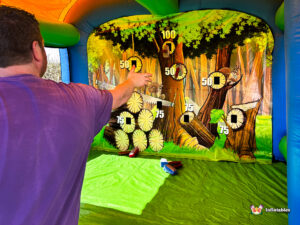 Follow-through shot of a participant throwing a foam axe at the inflatable target board, with several axes already on the floor of the arena.