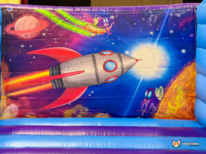 A close-up of the back wall mural inside the bouncer, depicting a silver rocket flying through space toward a bright star with small purple aliens.