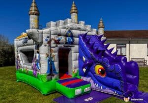 A colorful inflatable castle with a dragon-themed slide, featuring cartoon characters, towers, and a vibrant green base on a sunny day.